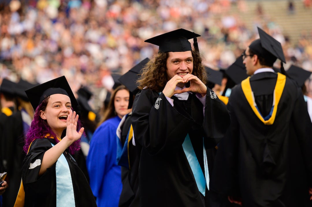 Graduates waving and gesturing to loved ones in graduation crowd