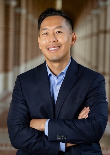 An Asian man in a suit smiles warmly at the camera