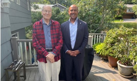 An older white man in flannel, Louis Brus, stands next to a black man in a suit, Reginald Desroches.
