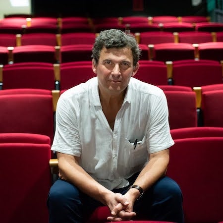 French intellectual Eric Fassin sitting inside a theater, wearing a white shirt and blue jeans