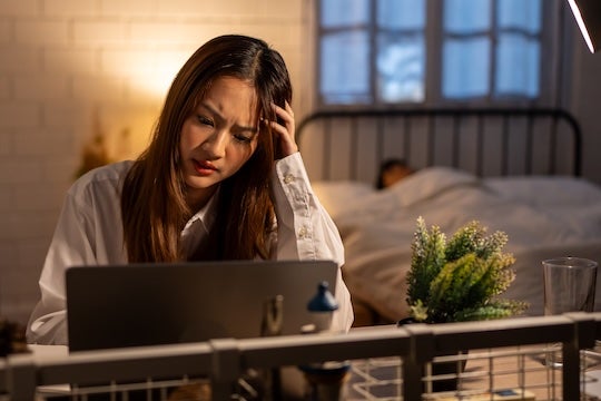 Overworking woman while husband sleeps.