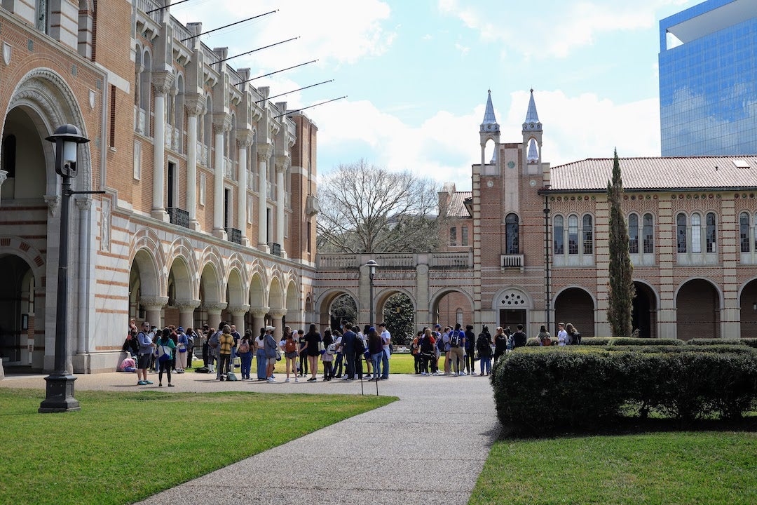 A group of high school students on a tour at Rice in the academic quad outside Lovett Hall.