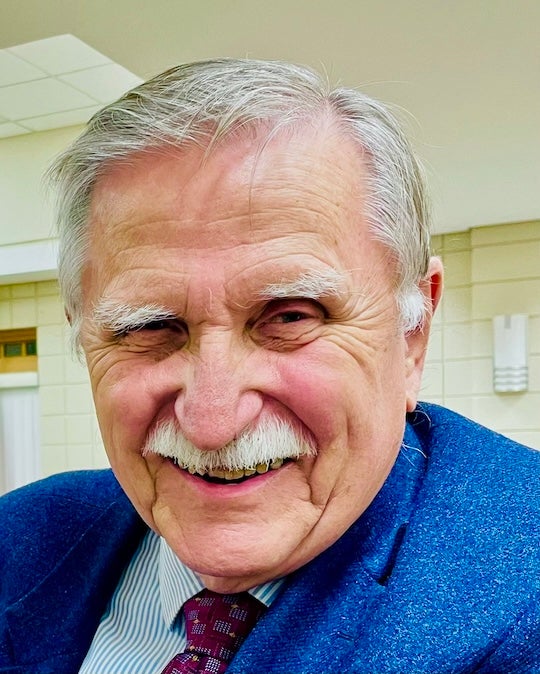 An older white man grins at the camera