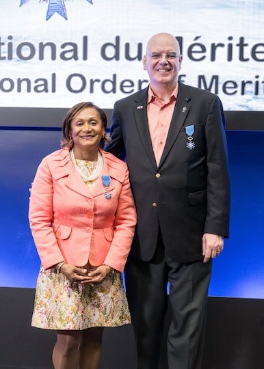 A short black woman stands next to a tall white man. Both are in formal dress and smiling