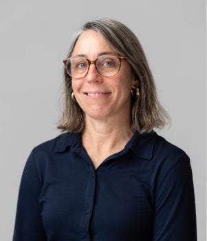 A white woman in glasses smiles at the camera