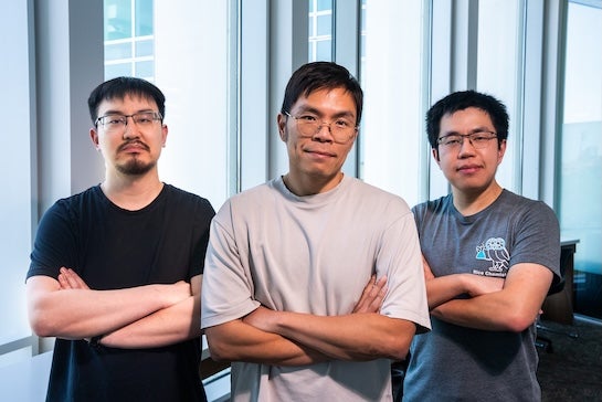 Three Asian men stand with their arms crossed in front of a window.