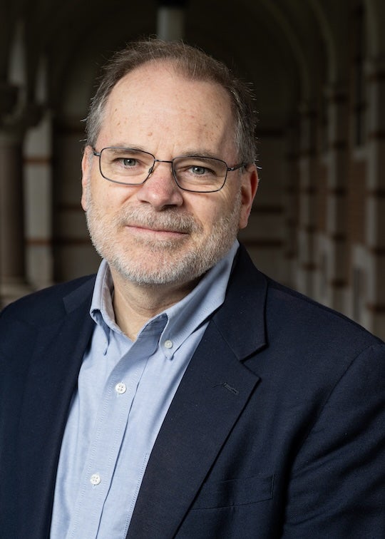 An older white man in a suit smiles gently at the camera. 