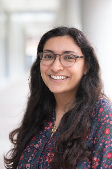 A woman stands in an outdoor hallway and smiles at the camera. 