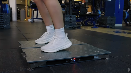 A soccer player stands on a force plate platform.