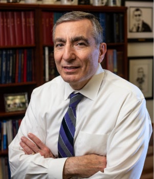 A white man stands in front of a bookshelf and smiles