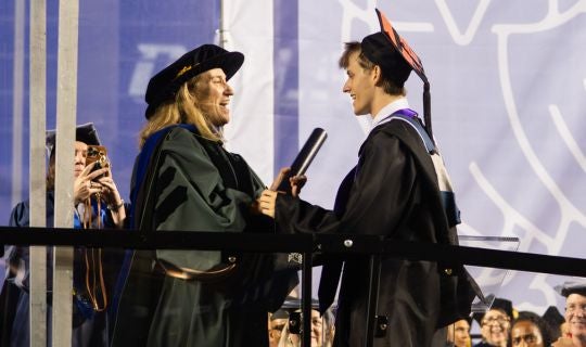 Mikki Hebl hands her son Jackson his diploma on stage