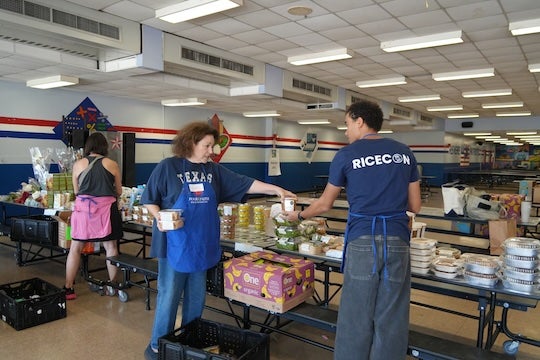 Rice senior Ian Wright helps volunteers arrange produce and prepared foods ahead of a Second Servings of Houston pop-up market serving families at Paul Revere Middle School.