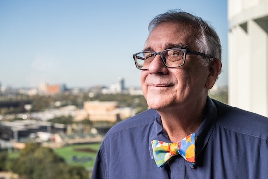 An older white man in a colorful bowtie stares off into the distance, smiling slightly