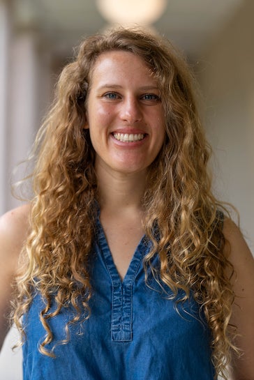 A white woman with curly hair stands outside.