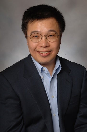 A Chinese man in a suit and glasses smiles at the camera