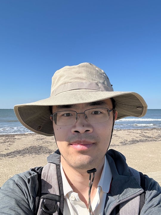 An Asian man in a park smiles at the camera