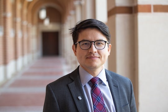 landscape photo of man in suit and tie facing the camera against a collonade