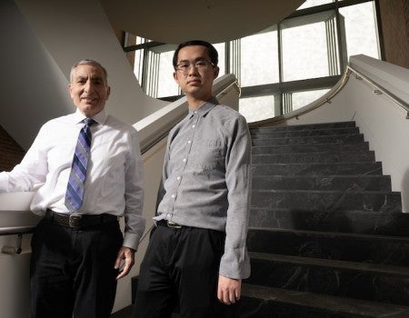 Two men, one older and white, one younger and Asian, stand at the bottom of a staircase