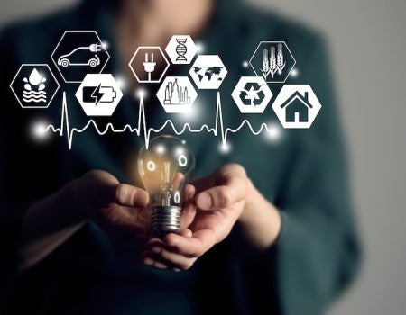 A woman holds a lightbulb. Above the lightbulb are graphics representing different sources of energy.