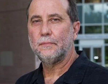 A white, older man with a white beard stares at the camera. 