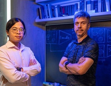 two researchers face the camera with arms crossed in front of a blackboard