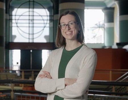 Woman in green shirt with white sweater with arms folded over her chest and smiling looks at the camera 