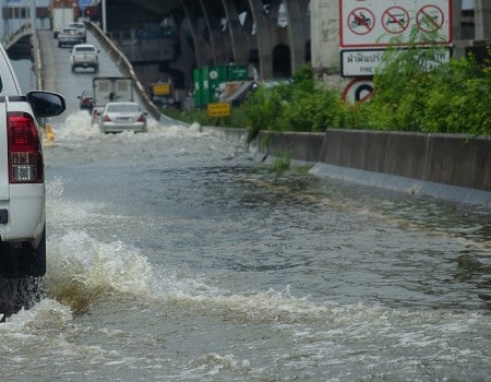 A truck drives through a flooded road, following a line of cars onto an elevated on-ramp