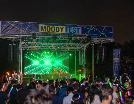 A picture of the Moody Fest stage and all the attendees listing to music and waving glow sticks.