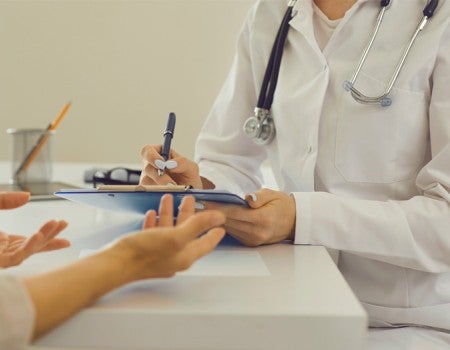 Female therapeutist with clipboard listening to patient and noting down her health complaints