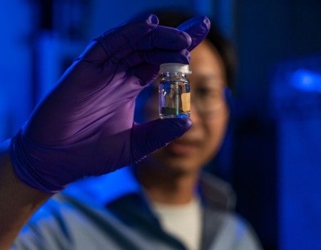 A jar with grey powder in it is held up by a slightly out of focus Asian man