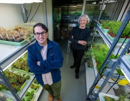 A young white man and older white woman stand in between shelves of plants