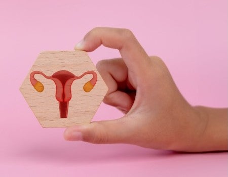 A white hand hold a hexagon tile on which is a picture of a uterus