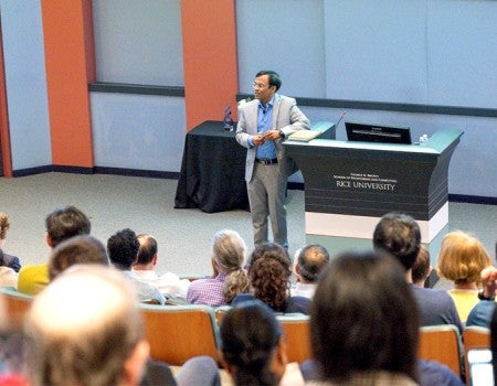 man in light gray suit standing next to lectern in front of a seated audience