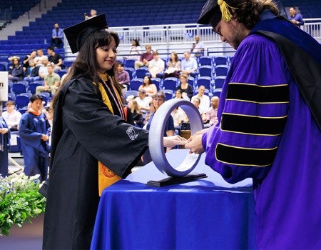 student in academic robes receives ring from professor
