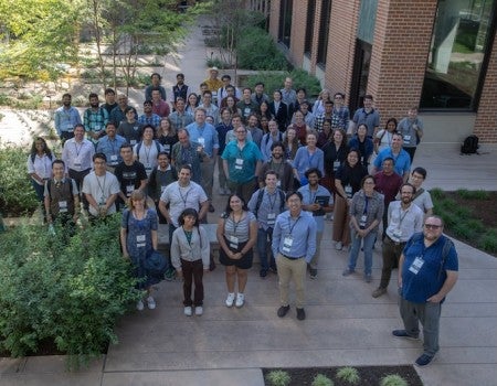 A group of people in blue and white shirts stand outside, all facing the camera
