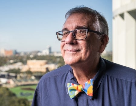 An older man with a colorful bowtie stares off into the distance, smiling