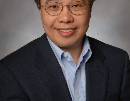 An Asian man in a suit smiles at the camera