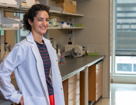 female researcher in lab coat leaning against lab bench