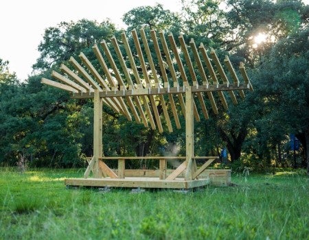 A wooden platform holds a picnic table with a leaf-shaped roof made of wooden slats
