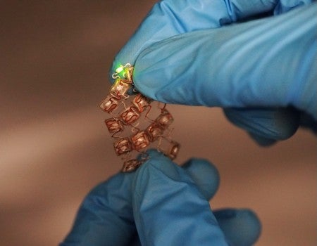 Stretchable moisture-activated battery held by two blue-gloved hands