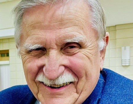 An older white man grins at the camera