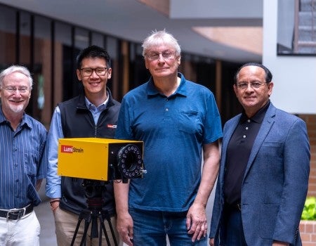 Four men stand outside around a yellow box. 
