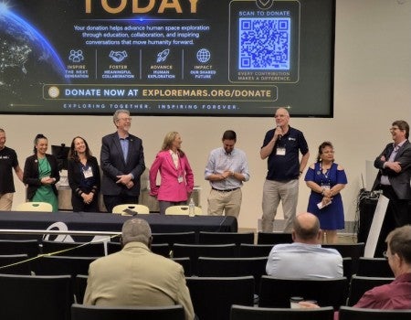 A group of people stand in front of an audience, talking and laughing. 