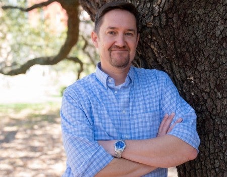 A while man stands in front of a tree and smiles