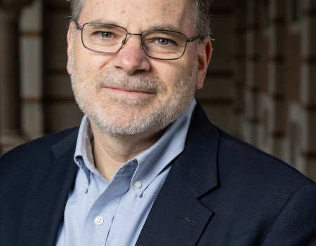An older white man in a suit smiles gently at the camera. 