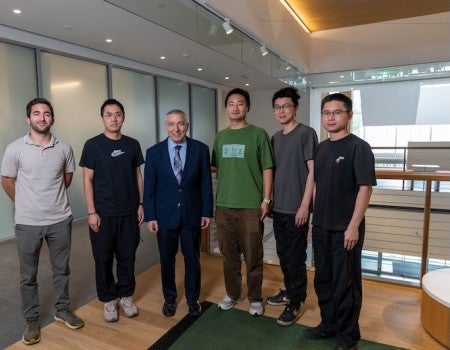 An older white man stands with five young Asian men. 