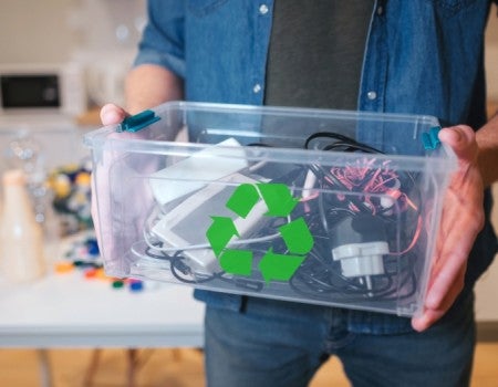 A white person holds a plastic bin full of electronic waste. 