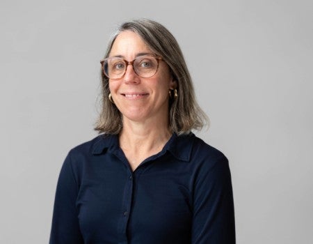 A white woman in glasses smiles at the camera