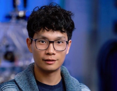 An Asian man in glasses smiles slightly.