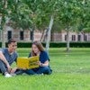 Students sitting on the lawn reading a book.